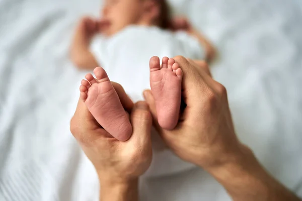 Bayi kaki di tangan ayah, kaki bayi yang baru lahir, bayi kecil terletak di tempat tidur bayi. — Stok Foto