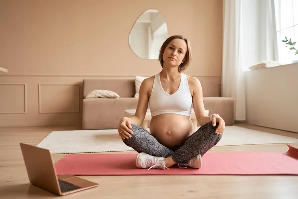Potret wanita hamil muda yang duduk di atas tikar yoga menonton latihan tutorial di rumah, menyalin ruang — Stok Foto