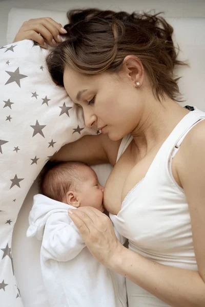 Hermosa mujer amamantando a su bebé en una acogedora casa en la cama. — Foto de Stock