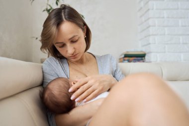 Bir anne bebeğini kollarında emziriyor. Beyaz kanepe, ev, beyaz üst