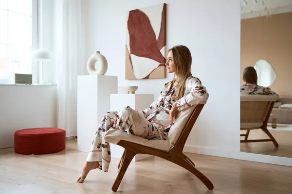 Jeune femme en pyjama de soie reposant et assis sur une chaise confortable à la maison — Photo