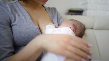 Annenin evdeki koltukta oturup bebeğini emzirdiği yakın plan.
