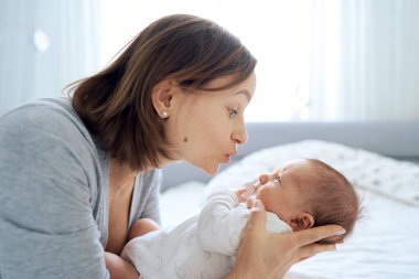 Bir aylık, tatlı bir çocuğun yatakta annesiyle oynamasına yakın. Annem oğlumla konuşuyor ve ona sarılıyor..