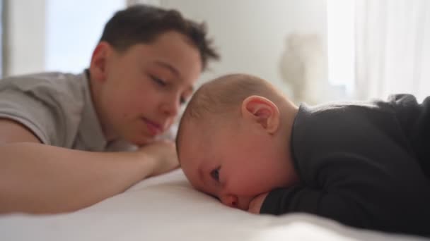 Feliz irmãozinho com o bebê recém-nascido deitado em uma cama juntos, beijando e abraçando. Bebê recém-nascido e irmão de três anos juntos. Com amor. Família. — Vídeo de Stock