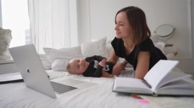 Küçük oğlu olan genç bir anne yatakta oturuyor ve laptopta çalışmaya çalışıyor.