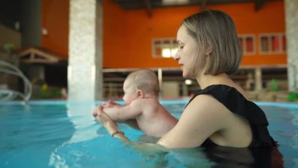 Мама вчить своє немовля плавати в закритому громадському басейні. Дитина кидається на штучну хвилю в аквапарку. — стокове відео