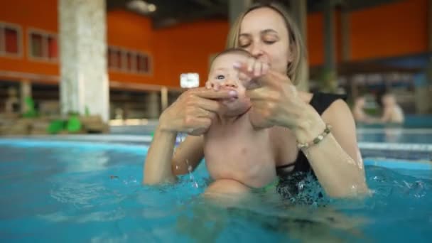 Anne bebeğine kapalı bir havuzda yüzmeyi öğretiyor. Çocuk, Aquapark 'ta yapay bir dalgada sallanıyor. — Stok video