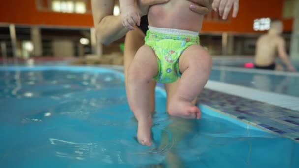 Mutter bringt ihrem Baby das Schwimmen in einem geschlossenen öffentlichen Schwimmbad bei. Das Kind schwingt auf einer künstlichen Welle im Aquapark — Stockvideo