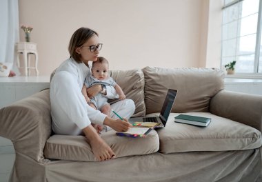 Dizüstü bilgisayarda çalışan genç bir anne. İş kadını evde küçük bir kızla çalışıyor. Doğum izninde çalış. Covid 19.