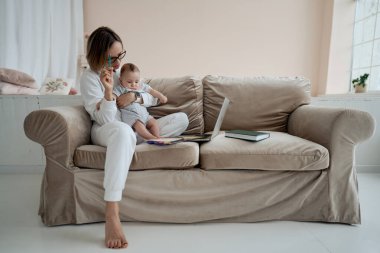 Dizüstü bilgisayarda çalışan genç bir anne. İş kadını evde küçük bir kızla çalışıyor. Doğum izninde çalış. Covid 19.