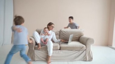 Çalışmayan bir atmosfer. Genç bir kadın dizüstü bilgisayarla çalışmaya çalışıyor ama çocukları kanepenin etrafında koşup onu rahatsız ediyor.