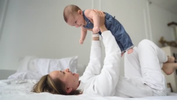 快乐健康的年轻成年高加索人妈妈抱着可爱的婴儿在床上玩飞机。可爱的高加索妈妈和可爱可爱的小儿子在舒适的卧室里做瑜伽体操. — 图库视频影像
