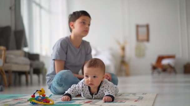 O irmão mais novo senta-se com o irmão mais novo. Criança Família com crianças em casa — Vídeo de Stock