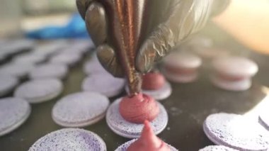 Evde badem kurabiyesi yapma süreci. Kadın pasta şefinin elinde ganache ve torbadan sıkılmış kırmızı meyve reçeli tutan el resimleri. Doğa çörekleri.