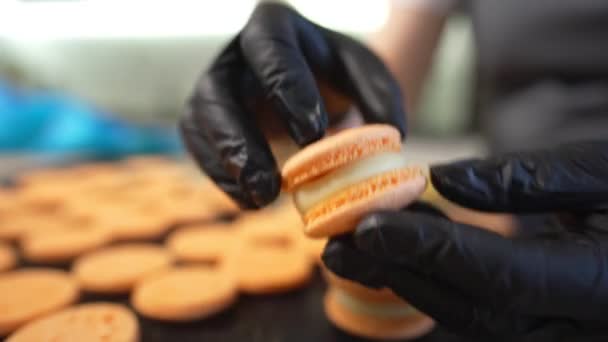 Prozess der Herstellung von Makronen zu Hause. Aufnahme von Händen einer Konditorin, die weißen Macaron mit Ganache in der Hand hält und rote Fruchtmarmelade aus der Tüte presst. Naturteigmakronen — Stockvideo