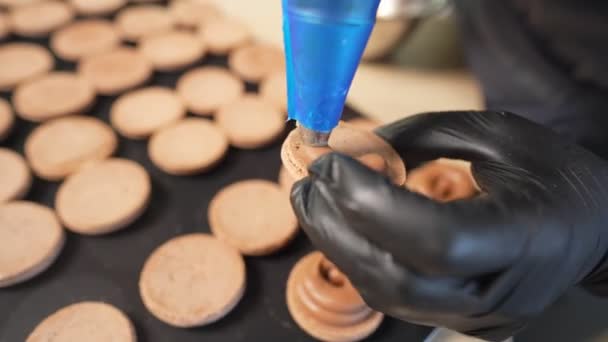 Proceso de hacer macarrones en casa. Tiro de manos de chef de pastelería femenina sosteniendo macaron blanco con ganache y exprimiendo mermelada de fruta roja de la bolsa. Macarrones de pastelería de la naturaleza — Vídeo de stock