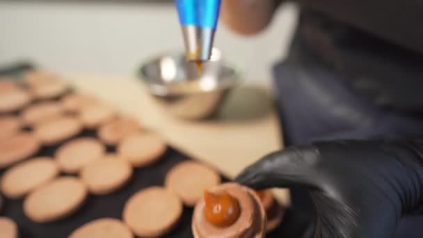 Prozess der Herstellung von Makronen zu Hause. Aufnahme von Händen einer Konditorin, die weißen Macaron mit Ganache in der Hand hält und rote Fruchtmarmelade aus der Tüte presst. Naturteigmakronen — Stockvideo