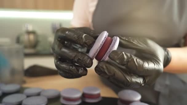 Prozess der Herstellung von Makronen zu Hause. Aufnahme von Händen einer Konditorin, die weißen Macaron mit Ganache in der Hand hält und rote Fruchtmarmelade aus der Tüte presst. Naturteigmakronen — Stockvideo