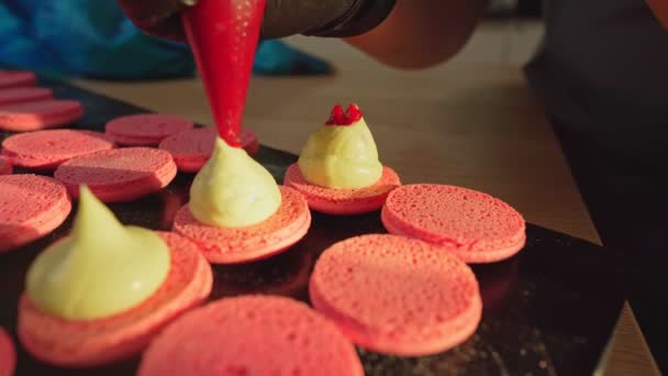 Proces výroby makarónů doma. Fotka ženských rukou šéfkuchařky, držící bílý macaron s ganache a mačkající červený ovocný džem z tašky. Přírodní pečivo makarony — Stock video