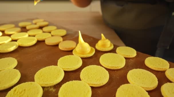 Proceso de hacer macarrones en casa. Tiro de manos de chef de pastelería femenina sosteniendo macaron blanco con ganache y exprimiendo mermelada de fruta roja de la bolsa. Macarrones de pastelería de la naturaleza — Vídeos de Stock