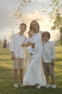 Anne ve üç çocuk sarılıyor. Mutlu bir aile dışarıda oturuyor: bir kadın ve iki kardeş çocuklar ve küçük şirin bir çocuk..