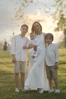 Anne ve üç çocuk sarılıyor. Mutlu bir aile dışarıda oturuyor: bir kadın ve iki kardeş çocuklar ve küçük şirin bir çocuk..