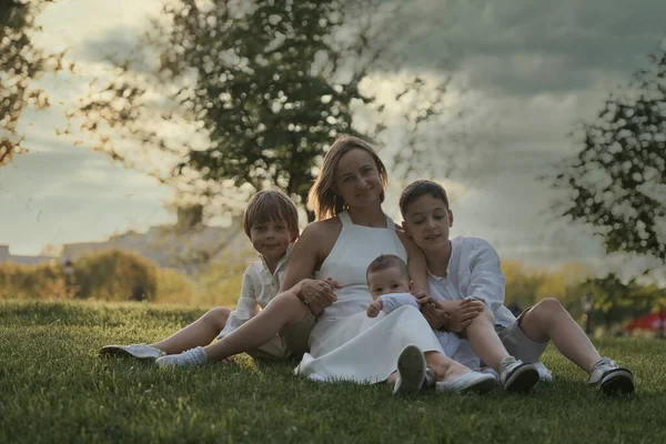 Mãe e três filhos abraçados. Família feliz sentado ao ar livre: mulher e dois irmãos meninos crianças e menino pequeno bonito. — Fotografia de Stock