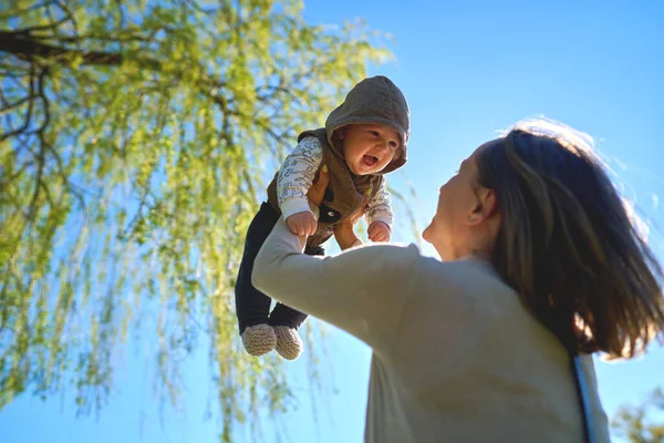 Silueta matky a dítěte při západu slunce. Matka vyhazuje dítě do vzduchu. — Stock fotografie