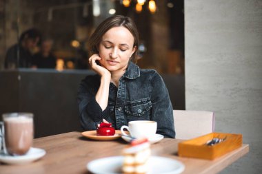 Bir kafedeki masada otururken bir parça kek yiyip kahve içen mutlu bir kadının portresi.