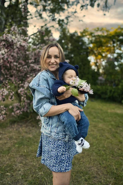 Mamma e bambino in giardino fiorito. Mamma e bambino in primavera. Scena familiare primaverile. Fiori di melo o ciliegio. — Foto Stock