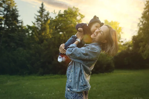 La madre vomita il bimbo, giocando e ridendo in giorno d'estate di sole su natura. Famiglia felice all'aperto. — Foto Stock