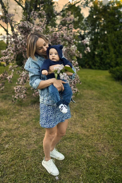 Mamma e bambino in giardino fiorito. Mamma e bambino in primavera. Scena familiare primaverile. Fiori di melo o ciliegio. — Foto Stock