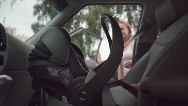 Madre joven que pone al bebé en el asiento del coche asegurando al niño para el viaje por carretera padre responsable que cuida la seguridad de los niños pequeños en el vehículo — Vídeos de Stock