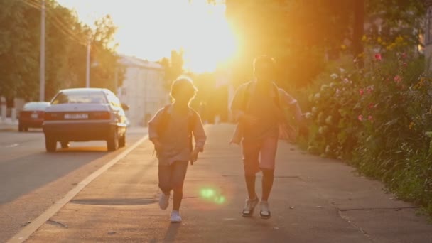 Två skolpojkar med ryggsäckar på gatan vid solnedgången. Tillbaka till skolan. — Stockvideo
