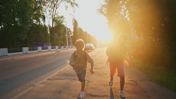 Två skolpojkar med ryggsäckar på gatan vid solnedgången. Tillbaka till skolan. — Stockvideo