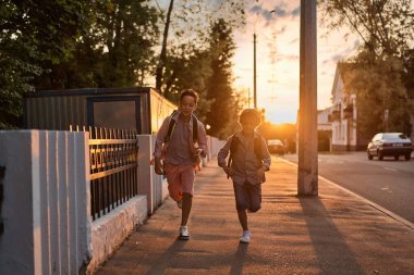 Gün batımında sokakta koşan sırt çantalı iki okul çocuğu. Okula geri dön..