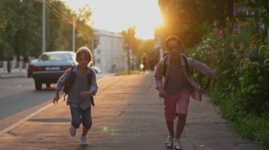 Gün batımında sokakta koşan sırt çantalı iki okul çocuğu. Okula geri dön..