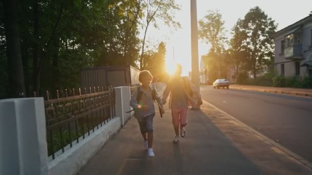 Két iskolás hátizsákkal az utcán szaladgál naplementekor. Vissza az iskolába.. — Stock videók