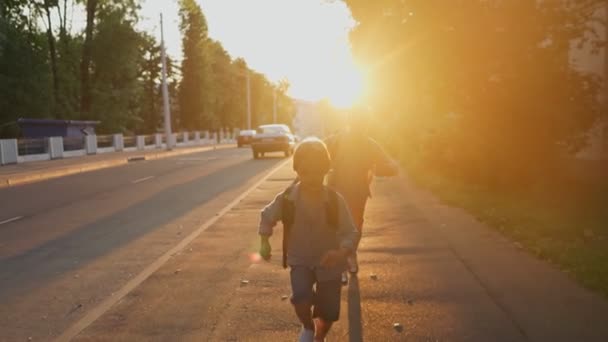 Zwei Schüler mit einem Rucksack laufen bei Sonnenuntergang über die Straße. Zurück zur Schule. — Stockvideo