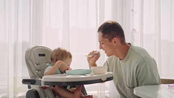 Father acting Mom feeding his son baby 1 on chair in the house. Fathers day — Stock Video