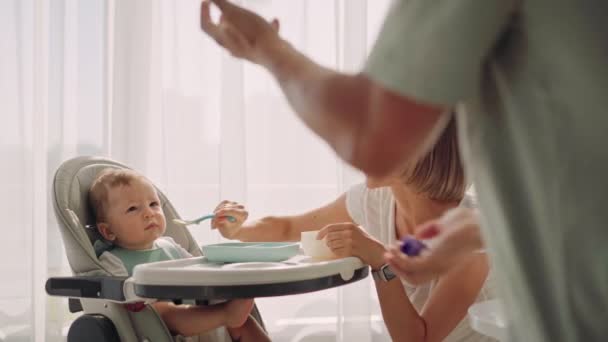 Pappa underhåller barnet under utfodring. Fadern jonglerar medan mamman matar barnet. Problemet med att mata ett barn — Stockvideo