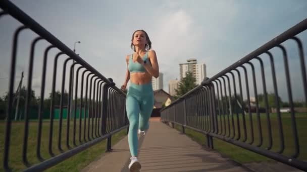 A fit young caucasian woman running intensively in slow motion on the bridge in the morning. Concept of a healthy lifestyle. Long shot of running woman. Vitality of sport. — Stock Video