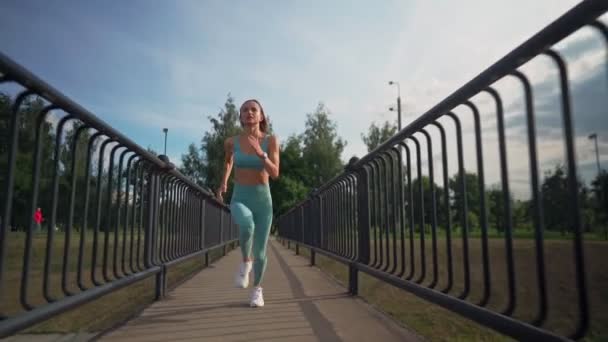 Une jeune femme caucasienne en forme courant intensément au ralenti sur le pont le matin. Concept de mode de vie sain. Longue chance de courir femme. Vitalité du sport. — Video