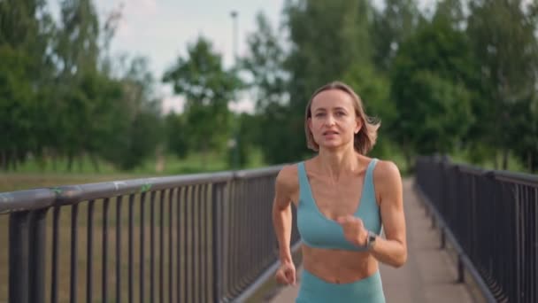 Una joven caucásica en forma que corre intensamente en cámara lenta en el puente por la mañana. Concepto de un estilo de vida saludable. Un tiro medio de mujer corriendo. Vitalidad del deporte. — Vídeo de stock