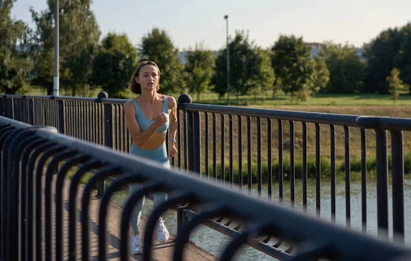 Een fitte jonge blanke vrouw die 's morgens in slow motion op de brug rent. Concept van een gezonde levensstijl. Een kleine kans op een vluchtende vrouw. Vitaliteit van de sport. — Stockfoto