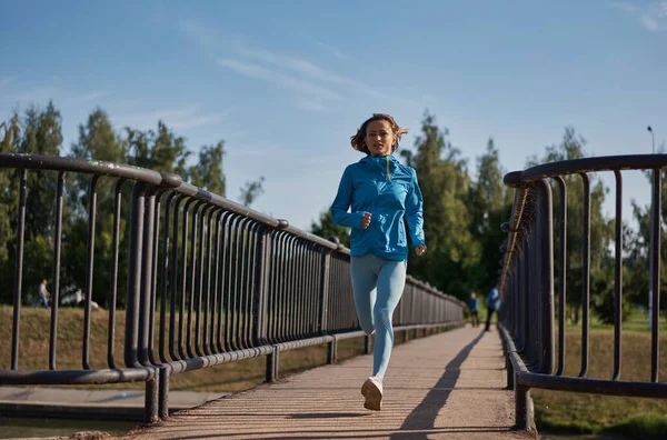 Zdolna młoda, kaukaska kobieta biegająca rano w zwolnionym tempie po moście. Koncepcja zdrowego stylu życia. Dalekie szanse na ucieczkę. Witalność sportu. — Zdjęcie stockowe