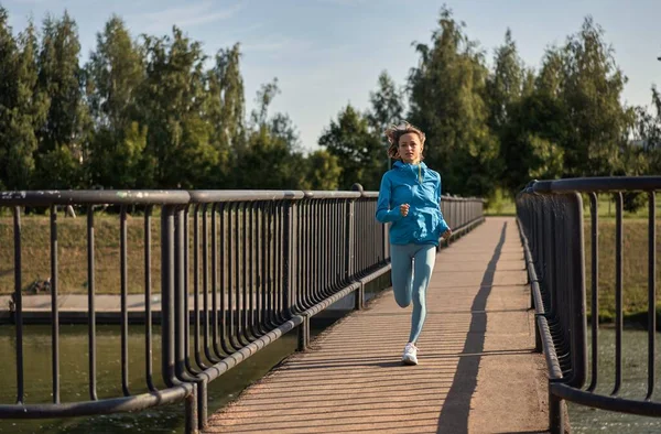 Een fitte jonge blanke vrouw die 's morgens in slow motion op de brug rent. Concept van een gezonde levensstijl. Een kleine kans op een vluchtende vrouw. Vitaliteit van de sport. — Stockfoto