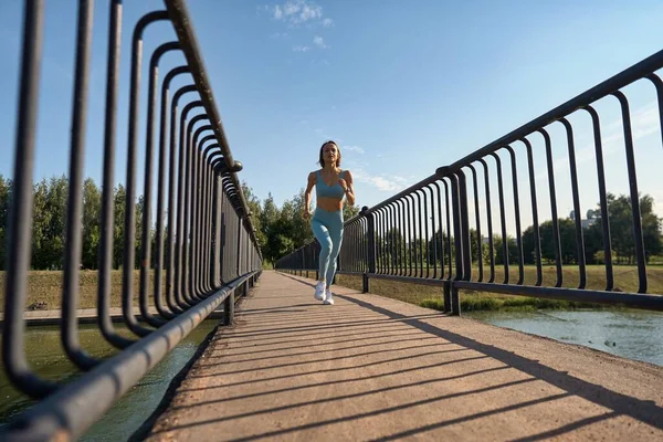 Een fitte jonge blanke vrouw die 's morgens in slow motion op de brug rent. Concept van een gezonde levensstijl. Een kleine kans op een vluchtende vrouw. Vitaliteit van de sport. — Stockfoto