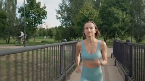 En vältränad ung kaukasisk kvinna som springer intensivt på bron på morgonen. Begreppet en hälsosam livsstil. En medelmåttig löpare. Idrottens vitalitet. — Stockvideo