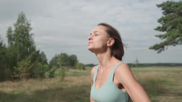 Foto de paralaje medio de mujer rubia caucásica trotando en el bosque en un día soleado. La corredora se detiene en la cima de la colina. Atleta enfocada mira al cielo — Vídeos de Stock